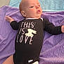 baby, black_clothing, bunny_graphic, child, concrete, cute, diaper, expression, face, freckles, head, infant, legs, lying_down, onesie, outdoor, purple_blanket, small_hands, soft_light, text_on_clothing