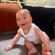 Mattéi a rejoint le concours — aidez-le/la à gagner de superbes lots ! baby, smiling, blue_eyes, sitting, couch, pillows, white_tank_top, plaid_shorts, beaded_necklace, happy, child, indoors, cozy, furniture, cute, skin, person, expression, home, playful