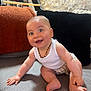 baby, smiling, blue_eyes, sitting, couch, pillows, white_tank_top, plaid_shorts, beaded_necklace, happy, child, indoors, cozy, furniture, cute, skin, person, expression, home, playful