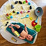 baby, child, towel, rug, wooden_floor, bath_toys, bucket, yellow_powder, plastic_toys, blue_shorts, indoor, baby_toy, smiling, playtime, cute, floor, child_playing, happy, infant, colorful