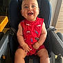 baby, child, smiling, stroller, red_clothing, blue_eyes, happy, indoor, seat, infant, cute, person, arms, legs, toy_car_pattern, lightning_bolt_pattern, high_chair, sitting, closeup, portrait
