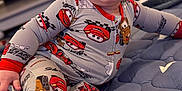 Jackson is registered to the contest to win money with this photo: baby, child, smiling, pajamas, clothing, foot, face, indoor, quilt, blanket, toy_car_pattern, happy, cute, toddler, person, sitting, home, living_room, infant, soft_lighting