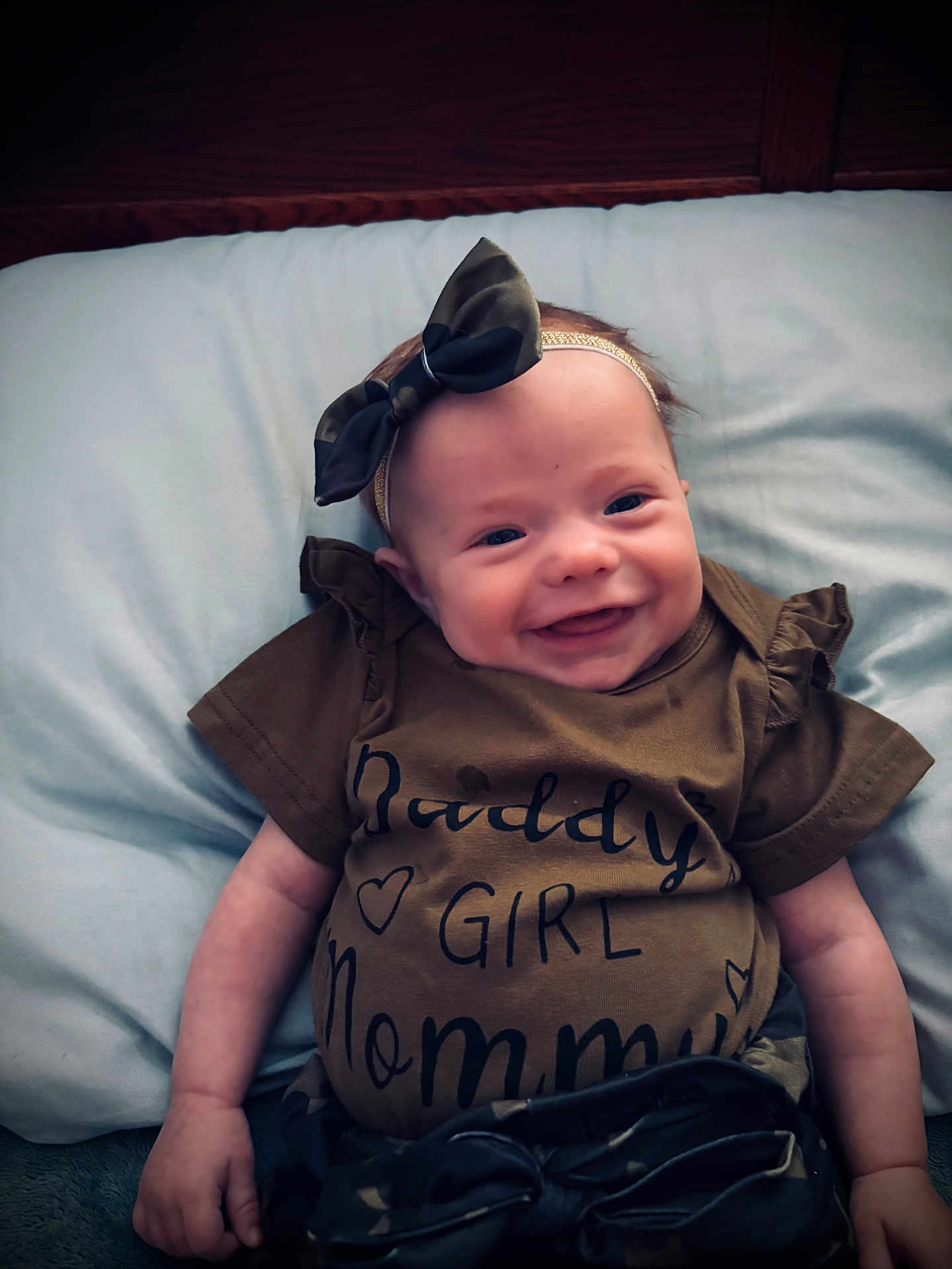Mia is registered to the contest to win money with this photo: baby, smiling, infant, headband, bow, clothing, pillow, bed, wooden_headboard, cute, happy, portrait, lying_down, child, toddler, apparel, fabric, face, skin, indoors