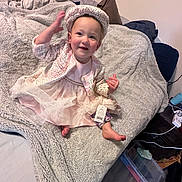Madelynn joined the competition — help win amazing prizes! toddler, child, smiling, dress, hat, blanket, bed, indoor, person, happy, cute, clothing, foot, hand, face, young_child, tag, fabric, cozy, home