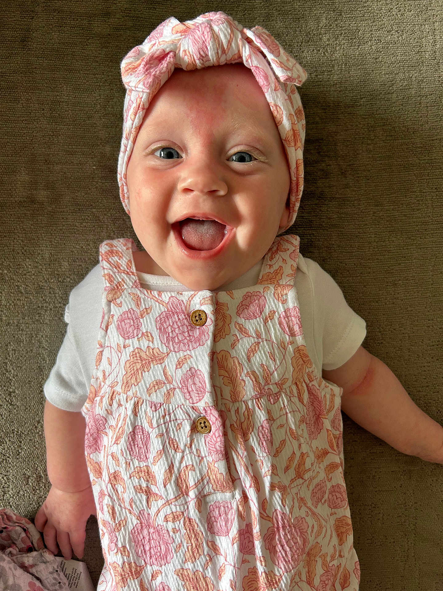 Penny joined the competition — help win amazing prizes! baby, infant, smiling, happy, face, headband, clothing, patterned, floral, cute, child, portrait, lying_down, skin, hand, white_shirt, button, fabric, texture, indoors