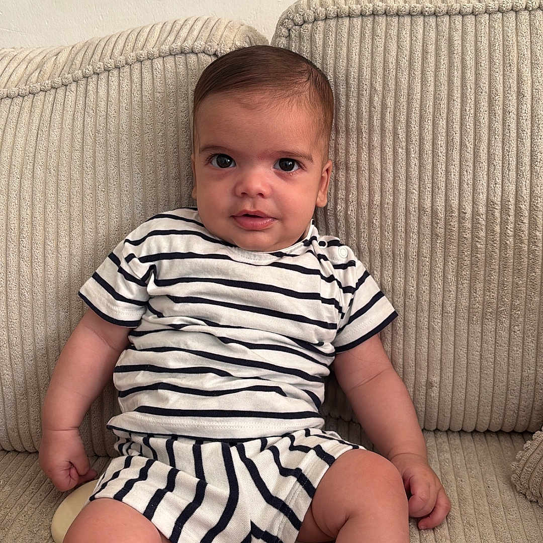 Islem participe au concours pour gagner de l'argent avec cette photo : arms, baby, beige, child, comfort, couch, curly_hair, cute, expression, face, furniture, indoor, infant, legs, portrait, relaxing, sitting, skin, smiling, striped_clothing