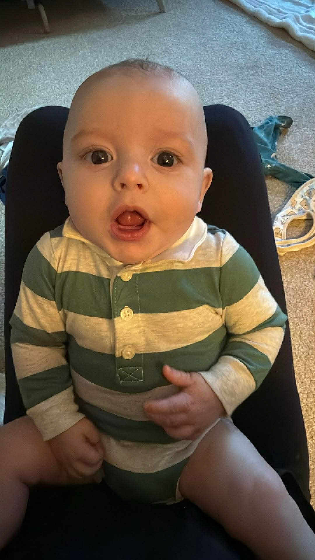 Rian is registered to the contest to win money with this photo: baby, infant, child, onesie, striped_clothing, sitting, legs, hands, face, eyes, mouth, surprised_expression, carpet, blanket, floor, indoors, furniture, lap, portrait, cute