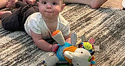 Addie is registered to the contest to win money with this photo: baby, child, plush_toy, rug, floor, wooden_floor, person, adult, legs, barefoot, casual, indoor, home, carpet, toy, colorful, crawling, cute, infant, relaxed