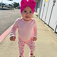 Blake is registered to the contest to win money with this photo: toddler, child, pink_bow, pajamas, outdoor, sidewalk, sunlight, happy, smile, footwear, clothing, person, cute, young_child, daytime, urban, shadow, headwear, walking, playful