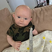 Arkin is registered to the contest to win money with this photo: baby, child, couch, blanket, camouflage_clothing, indoor, face, expression, holding, furniture, person, home, pacifier_clip, smiling_stars, moons, earring, head, skin, cute, seated