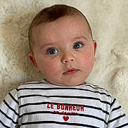 Milann a rejoint le concours — aidez-le/la à gagner de superbes lots ! baby, infant, face, blue_eyes, striped_shirt, text_on_clothing, heart, lying_down, blanket, soft_texture, closeup, portrait, cute, child, person, apparel, casual_clothing, indoor, expression, young
