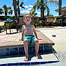 barefoot, blue_sky, boy, chairs, child, daytime, happy, holiday, outdoor, palm_trees, patio, pool, recreation, relaxing, smiling, summer, sunny, swimming_trunks, vacation, water