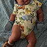 baby, infant, child, onesie, mittens, shoe, blanket, smiling, tongue_out, cute, animal_print, lying_down, soft_texture, playful, happy, indoors, small, adorable, cozy, portrait