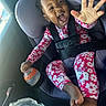 child, toddler, baby, car_seat, car, harness, safety_belt, smiling, laughing, open_mouth, reaching, hand, bottle, floral_clothing, hello_kitty, pink, outdoor_light, vehicle_interior, portrait, happy