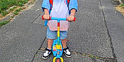 Chilo participe au concours pour gagner de l'argent avec cette photo : child, scooter, smile, outdoor, backpack, pavement, grass, shorts, sneakers, happy, person, topknot, play, daytime, urban, path, casual_clothing, fun, young, standing