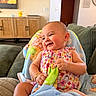 apparel, baby, blanket, child, colorful, couch, cozy, cute, furniture, happy, home, indoors, infant, living_room, person, playful, portrait, seated, smiling, toddler