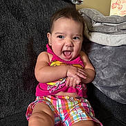 Isabella is registered to the contest to win money with this photo: toddler, child, smiling, happy, sitting, indoors, couch, blanket, colorful_clothing, pink_top, plaid_shorts, face, hands, short_hair, earrings, cozy, home, expression, joy, infant