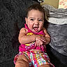 blanket, child, colorful_clothing, couch, cozy, earrings, expression, face, hands, happy, home, indoors, infant, joy, pink_top, plaid_shorts, short_hair, sitting, smiling, toddler