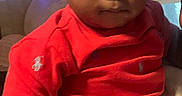 Amari is registered to the contest to win money with this photo: adult_hand, baby, blinds, blue_light, brown_skin, casual_photo, child, close_up, couch, curly_hair, family, indoors, infant, living_room, polo_shirt, portrait, red_shirt, serious_expression, sitting, window