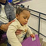 toddler, child, adult, stadium_seat, purple_seat, indoor, railing, person, curious, pigtails, jacket, sunglasses, supporting, people, sports_venue, concrete_floor, white_wall, hand, casual_clothing, event