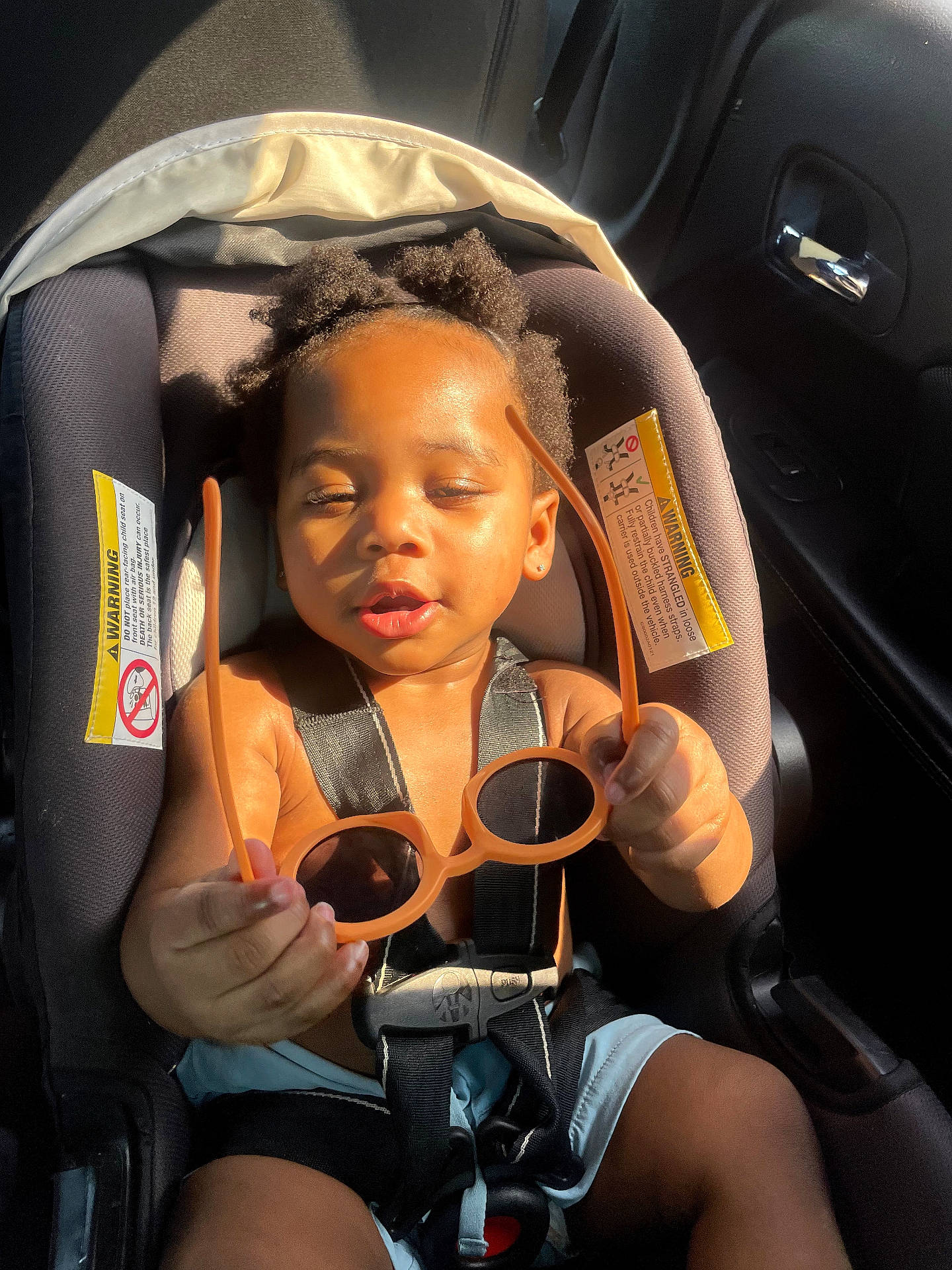 Fasha Douglas is registered to the contest to win money with this photo: baby, black_hair, car_door, car_interior, car_seat, child, curly_hair, cute, holding, infant, orange, portrait, seat, seatbelt, small_hands, summer_clothing, sunglasses, sunlight, sunshine, toddler