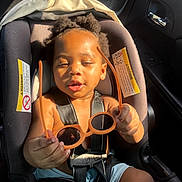 Fasha Douglas is registered to the contest to win money with this photo: toddler, child, car_seat, sunglasses, holding, sunlight, car_interior, seatbelt, black_hair, curly_hair, orange, summer_clothing, baby, infant, seat, portrait, cute, sunshine, small_hands, car_door
