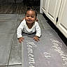 baby, child, smiling, kitchen, floor, mat, home, happy, person, indoor, tile_floor, white_clothing, hair_buns, candid, cute, infant, young_child, cabinet, floor_mat, portrait