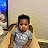 toddler, child, baby, sitting, chair, plush_chair, dog_ears, gray_shirt, little_dude, indoor, carpet, wall, mirror, reflection, curly_hair, expression, looking_at_camera, home, cozy, comfortable