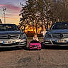 asphalt, center_composition, child, cute_child, family_scene, front_view, license_plate, luxury_car, mercedes, outdoor, parking_lot, pink_toy_car, portrait, sedan, small_driver, sunset, toddler, toy_car, trees, vehicle