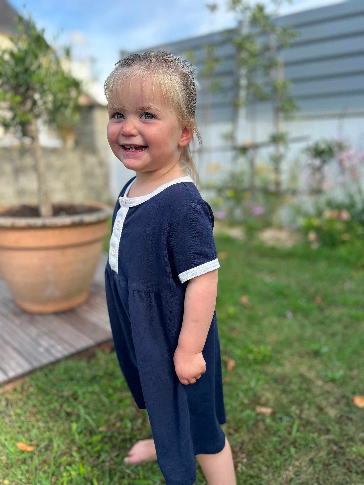 Charlotte a rejoint le concours — aidez-le/la à gagner de superbes lots ! child, girl, smiling, outdoor, grass, barefoot, dress, blond_hair, garden, potted_plant, greenery, happy, portrait, nature, yard, casual_clothing, daylight, cute, young, playful