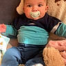 baby, pacifier, blue_sweater, pants, blanket, plush_toy, infant, indoor, child, cute, soft_toys, cozy, warm_lighting, sitting, portrait, young_child, face, head, clothing, comfortable