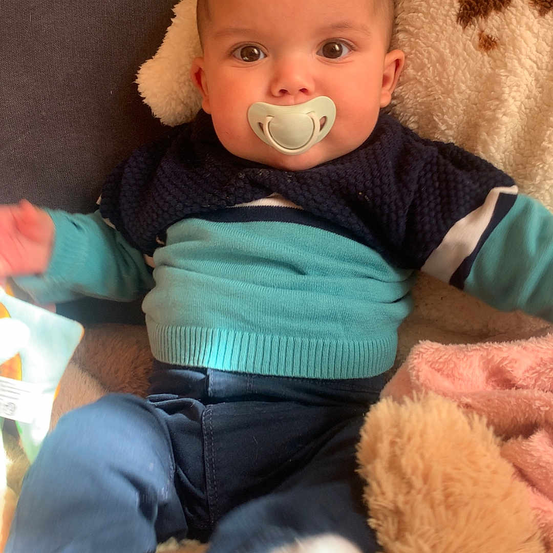 Menzo a rejoint le concours — aidez-le/la à gagner de superbes lots ! baby, pacifier, blue_sweater, pants, blanket, plush_toy, infant, indoor, child, cute, soft_toys, cozy, warm_lighting, sitting, portrait, young_child, face, head, clothing, comfortable