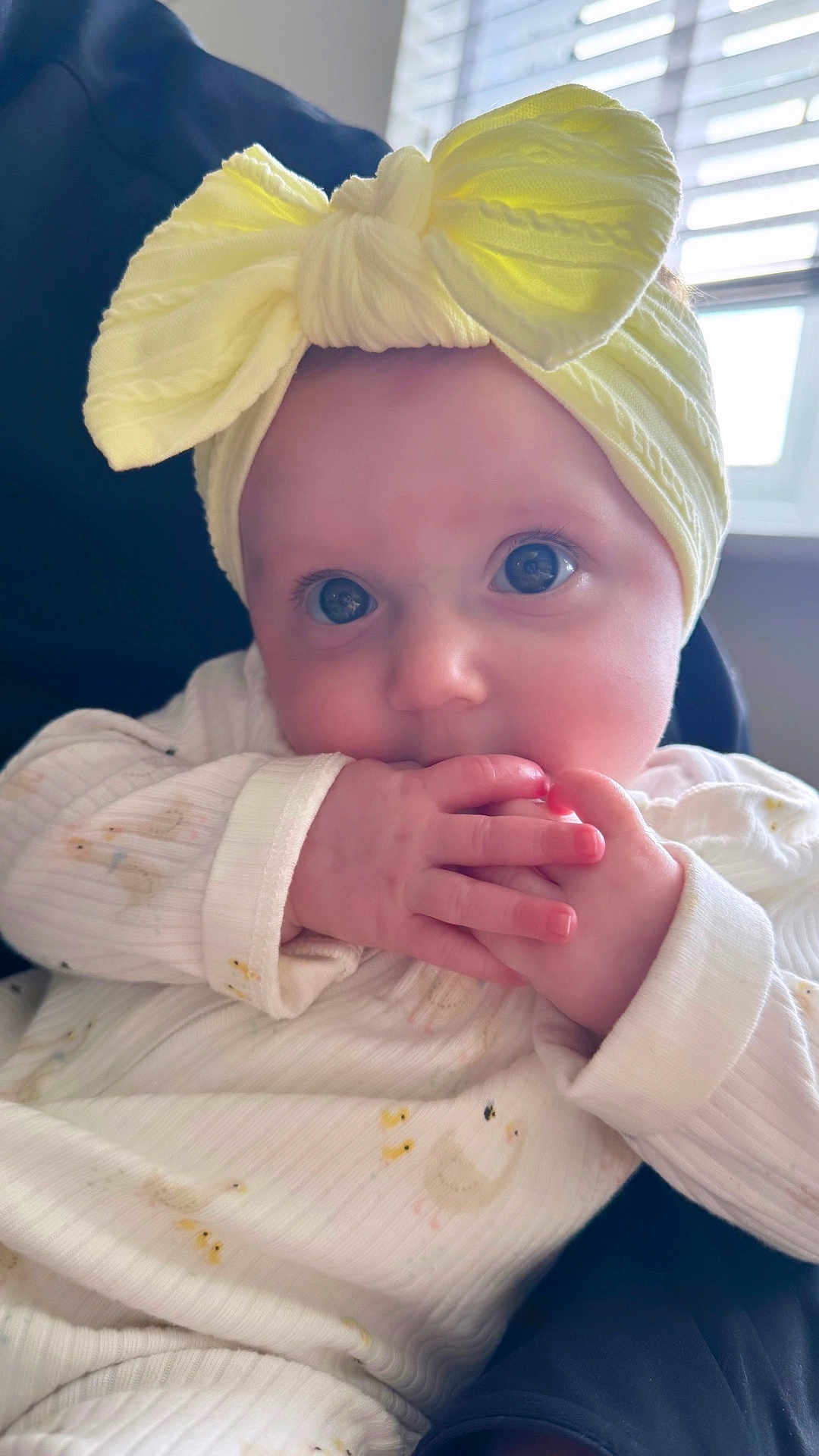 Flo joined the competition — help win amazing prizes! baby, infant, child, headband, yellow_bow, hands, fingers, sucking, white_outfit, duck_pattern, close_up, face, eyes, curious, sitting, chair, window, natural_light, indoor, portrait