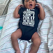 Amir is registered to the contest to win money with this photo: baby, infant, child, onesie, clothing, text, blanket, striped, lying_down, arms_up, expression, mouth_open, feet, hands, indoor, cushion, fabric, cute, humor, person