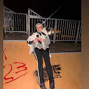 Moses is registered to the contest to win money with this photo: person, dog, skate_ramp, night, graffiti, fence, flash, casual_clothing, smiling, black_pants, sneakers, outdoor, pet, holding, happy, headband, long_hair, black_and_white, metal, urban