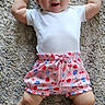 Gwen joined the competition — help win amazing prizes! baby, infant, carpet, clothing, onesie, pink_shorts, patterned_shorts, happy, smiling, arms_up, barefoot, cute, child, lying_down, indoors, person, skin, head, legs, toddler