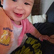 Gwen is registered to the contest to win money with this photo: baby, child, smile, face, pink_clothing, orange_clothing, cartoon, indoor, person, cute, happy, closeup, infant, young_child, apparel, hand, couch, blanket, wall, portrait