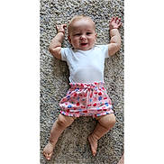 Gwen joined the competition — help win amazing prizes! baby, child, infant, smile, white_onesie, colorful_shorts, carpet, cute, happy, lying_down, arms_up, barefoot, patterned_clothing, indoor, portrait, skin, head, legs, feet, person