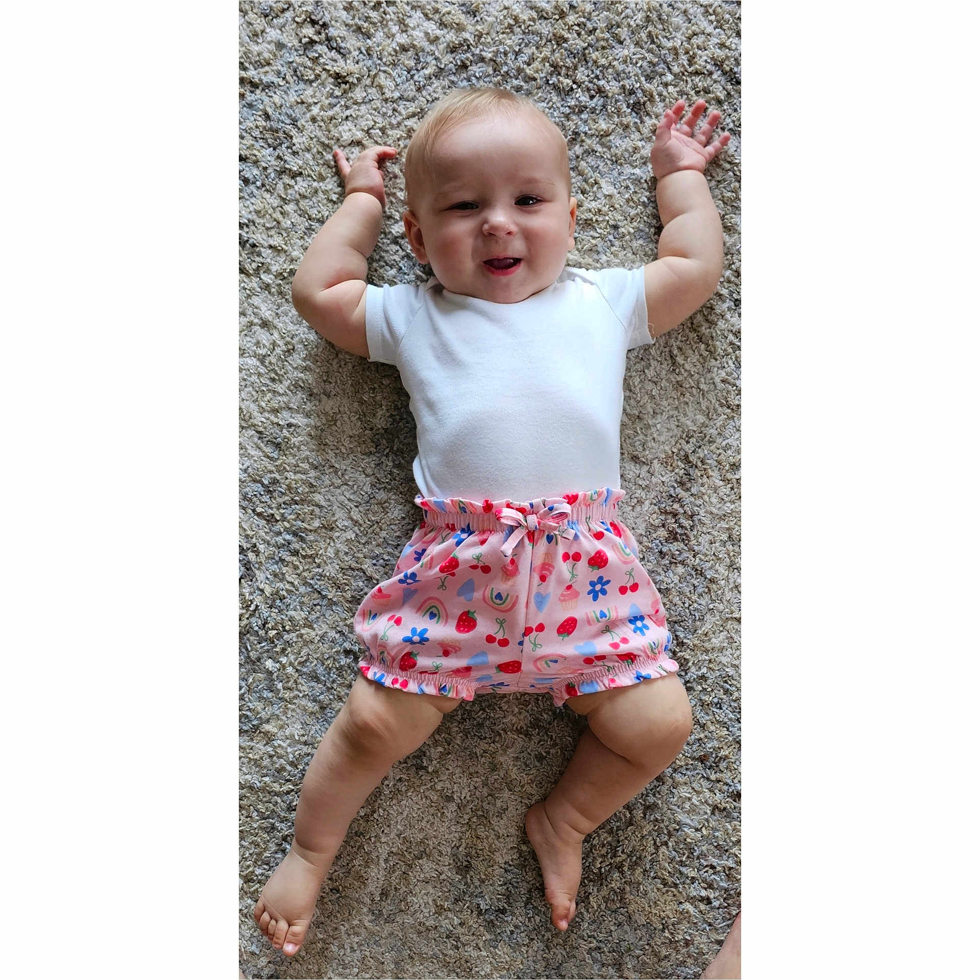Gwen joined the competition — help win amazing prizes! baby, child, infant, smile, white_onesie, colorful_shorts, carpet, cute, happy, lying_down, arms_up, barefoot, patterned_clothing, indoor, portrait, skin, head, legs, feet, person