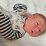 Noah is registered to the contest to win money with this photo: baby, newborn, infant, child, blanket, clothing, onesie, striped, animal_print, face, head, skin, lying_down, cute, soft, bed, expression, portrait, small, human