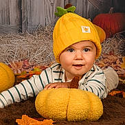 Tiago a rejoint le concours — aidez-le/la à gagner de superbes lots ! baby, child, hat, yellow_hat, plush_pumpkin, autumn_leaves, brown_rug, striped_shirt, fall_decor, cute, smiling, indoors, portrait, cozy, seasonal, soft_toys, pumpkins, happy, young_child, headwear