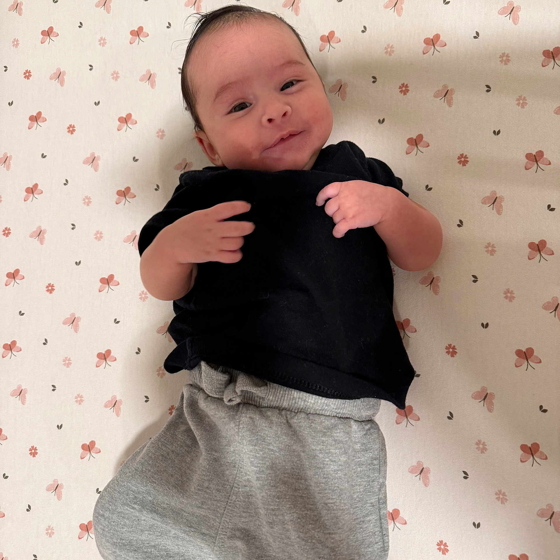 Twisha joined the competition — help win amazing prizes! baby, black_shirt, blanket, casual_clothing, cute, face, floral_pattern, grey_pants, happy, head, indoors, infant, lying_down, person, portrait, skin, small_hands, smiling, soft_light, young_child