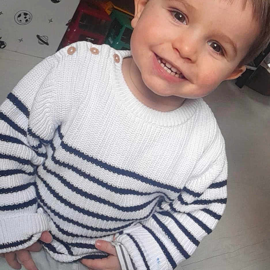 Léo participe au concours pour gagner de l'argent avec cette photo : baby, bodypart, clothing, face, happy, head, indoors, knitwear, longsleeve, mouth, pants, person, photography, portrait, shirt, sitting, sleeve, smile, sweater, teeth