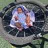 Reign is registered to the contest to win money with this photo: baby, child, swing, playground, blanket, blue_clothing, headband, smiling, outdoor, sunlight, rope, green_turf, infant, happy, one_piece, legs, feet, relaxing, toy, summer