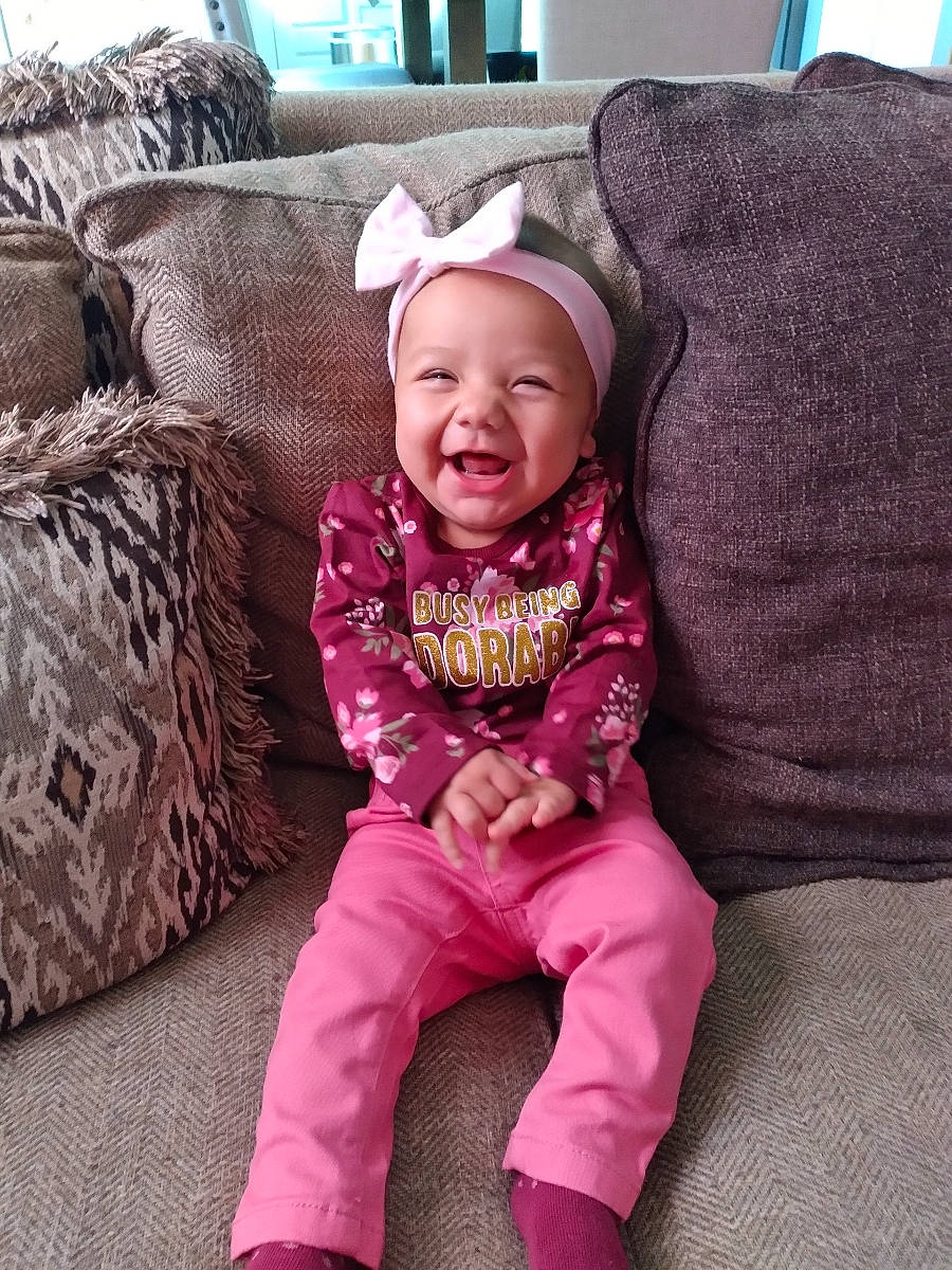 Harlowe is registered to the contest to win money with this photo: baby, baby_toddler_clothing, child, comfort, couch, eye, face, happy, head, headgear, headwear, lap, magenta, outerwear, person, pink, purple, sitting, sleeve, smile