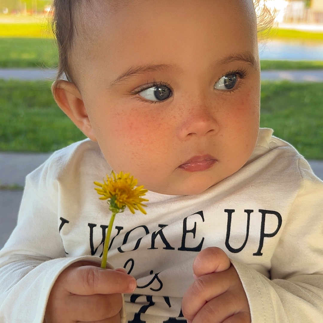 Irilynn is registered to the contest to win money with this photo: baby_hands, casual_clothing, child, cute, dandelion, daylight, expression, face, flower, freckles, grass, nature, outdoor, pink_shorts, polka_dots, portrait, sitting, toddler, white_shirt, young_child