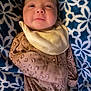 baby, infant, newborn, blanket, patterned_blanket, bib, onesie, clothing, face, cheeks, eyes, smile, portrait, closeup, lying_down, bedding, soft_texture, cozy, indoor, person