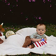 Stetson joined the competition — help win amazing prizes! baby, blanket, grass, outdoor, toy, plush_bull, cowboy_hat, american_flag, craft, child, greenery, purple_flowers, shirt, pants, foot, nature, cute, sitting, grass_field, playtime