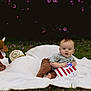 baby, blanket, grass, outdoor, toy, plush_bull, cowboy_hat, american_flag, craft, child, greenery, purple_flowers, shirt, pants, foot, nature, cute, sitting, grass_field, playtime