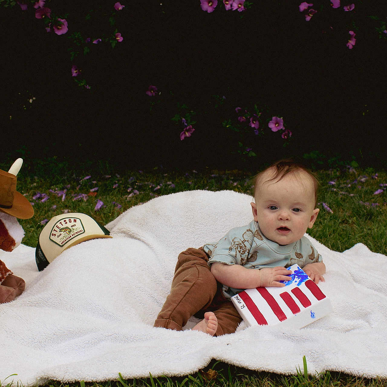 Stetson joined the competition — help win amazing prizes! american_flag, baby, blanket, child, cowboy_hat, craft, cute, foot, grass, grass_field, greenery, nature, outdoor, pants, playtime, plush_bull, purple_flowers, shirt, sitting, toy